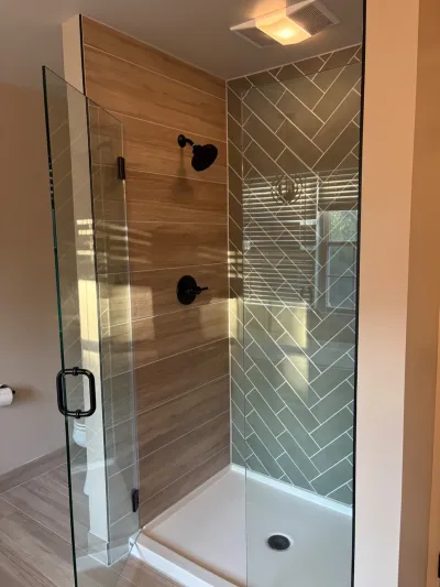 Walk-in glass shower with wood-look tile on one wall and herringbone gray tile on another, black fixtures.