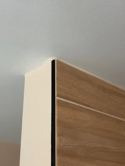 Close-up of a corner where a painted wall meets a wood-grain panel wall with a black trim strip.