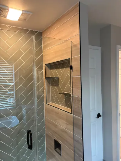 Modern shower with herringbone tile, wood-look tile wall, glass enclosure, and a black-trimmed tiled niche.