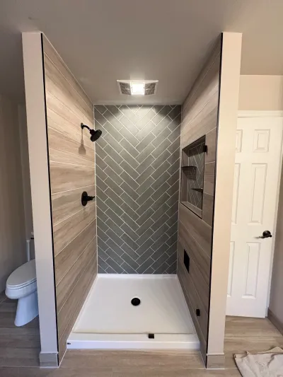 Walk-in shower with wood-look tile walls, a grey herringbone accent wall, and matte black fixtures.