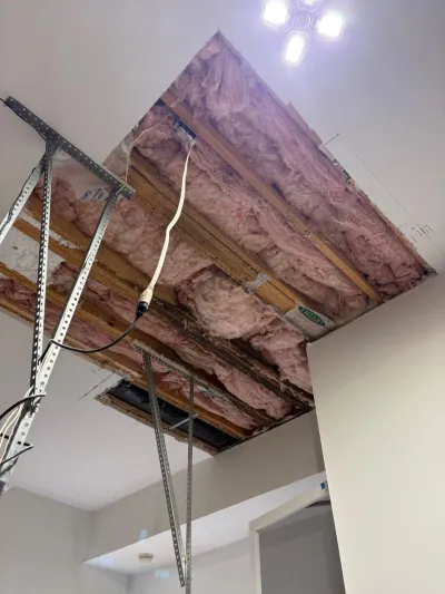 Open ceiling section during repair showing exposed insulation, joists, and wiring with support bracing.
