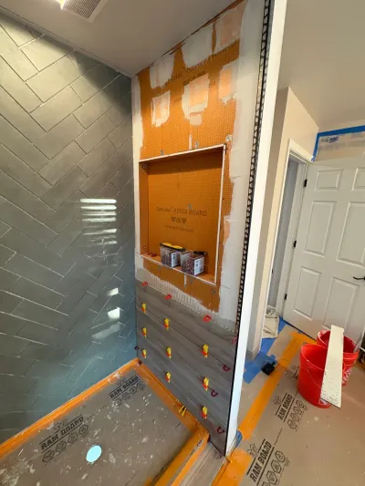 A shower under construction with herringbone tile on one wall and waterproofing membrane exposed on another.