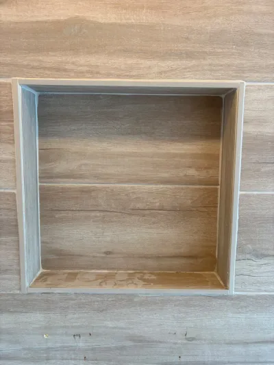 Close-up of a tiled shower niche with a center shelf, finished in wood-look porcelain tile.