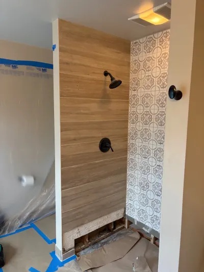 Shower under construction with wood-look tile and patterned accent tile, black fixtures, and exposed backer board at the base