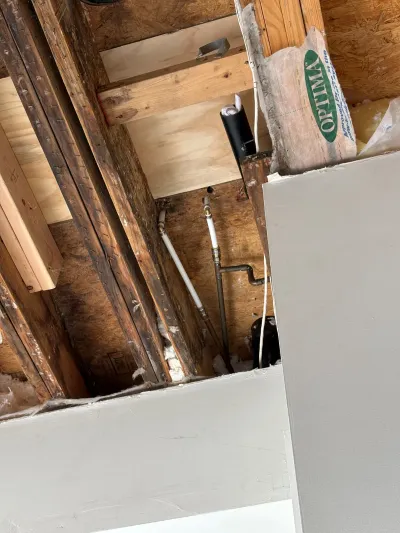 Open wall framing during renovation with water-stained studs, rough plumbing lines, and insulation.