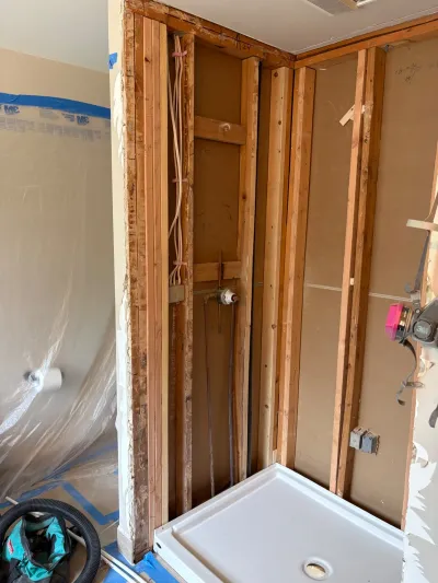 A bathroom shower area gutted to exposed wood framing with plumbing rough-in and a new shower base installed.