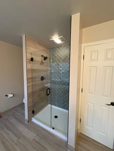 Walk-in shower with herringbone tile, wood-look tile walls, glass door, and matte black fixtures.