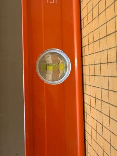 Close-up of a level's bubble vial checking alignment near a gridded tile backer board.