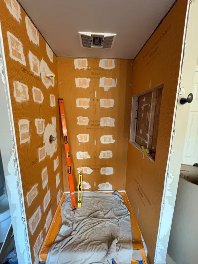 Shower stall mid-renovation with orange waterproofing membrane and rough-in for a niche and plumbing.
