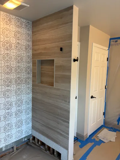 A bathroom shower under construction with patterned tile and wood-look plank tile, adjacent to a protected hallway.