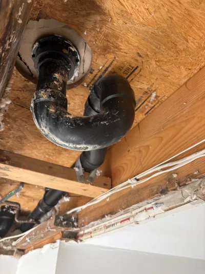 Exposed plumbing drain pipe and wiring beneath an unfinished basement ceiling during renovation work.