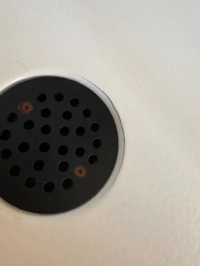 Close-up of a matte black perforated shower drain cover set into a light-colored shower base.