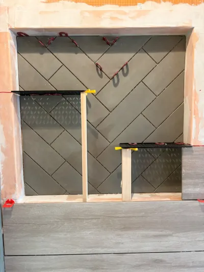 A shower niche under construction with herringbone tile held in place by clips and wood braces.