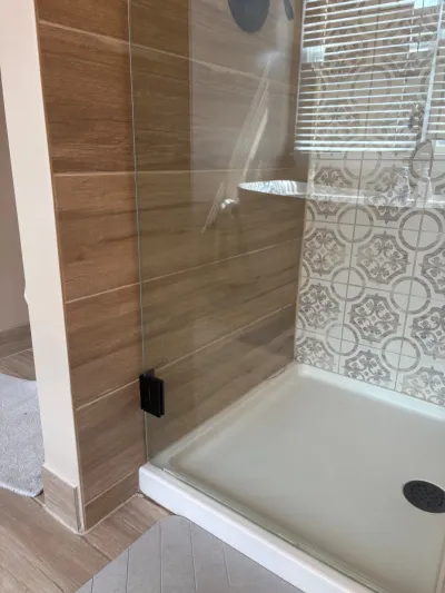 A tiled walk-in shower with wood-look tile, a patterned accent wall, and a frameless glass door.