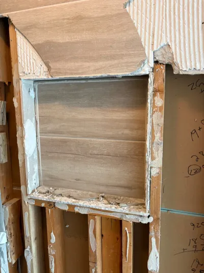 Exposed wall framing during a renovation, revealing a laminate-lined niche and pencil measurement notes on drywall.