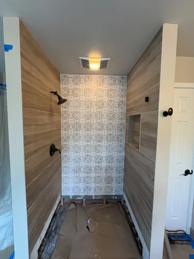A shower under construction with wood-look tile walls and a patterned tile accent wall, floor not yet finished.