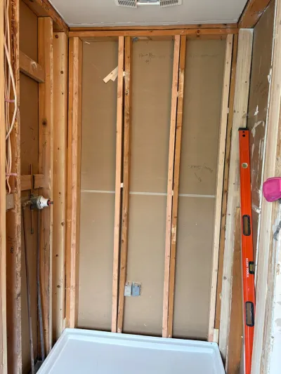 Gutted shower stall mid-renovation with exposed studs, rough-in plumbing, and a new shower pan on the floor.