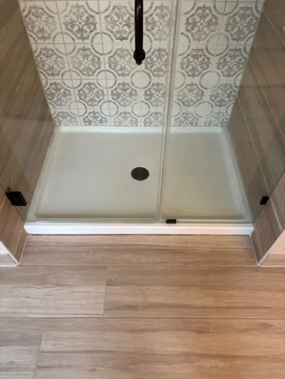 A tiled walk-in shower with a decorative patterned accent wall and glass door with a bronze handle.
