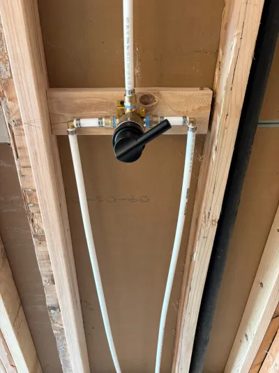 Close-up of a matte black shower valve rough-in plumbed with PEX piping in an open wall cavity.