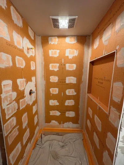 A shower stall mid-renovation with orange waterproof tile backer boards and a built-in niche, ready for tile.