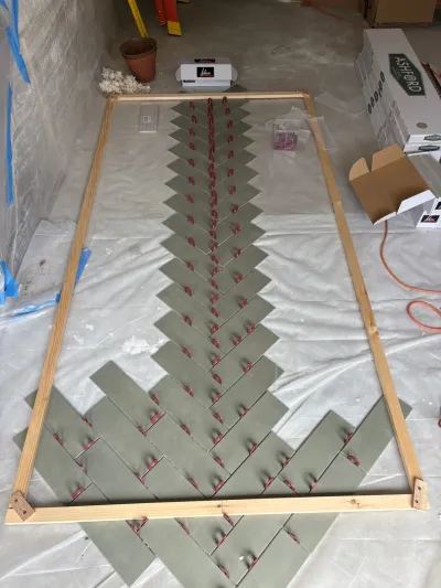 Sage green tiles dry-laid in a herringbone pattern inside a wooden frame on a protected concrete floor.