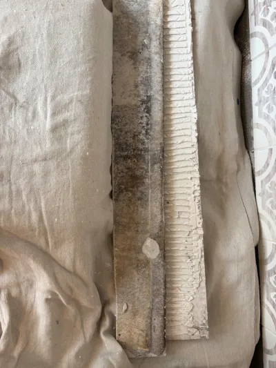 Close-up of a stained tile edge with ridged mortar residue resting on a canvas drop cloth.