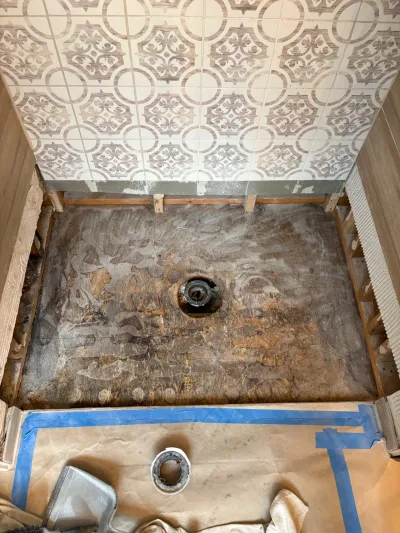 Bathroom shower floor mid-renovation showing exposed waterproofing membrane below finished patterned wall tile.