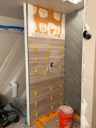 Shower under renovation with wood-look tile, leveling clips, and gray herringbone tile on the adjacent wall.