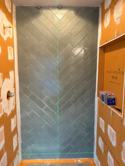 A shower stall mid-renovation with herringbone tile on the back wall and waterproofing board on the sides.