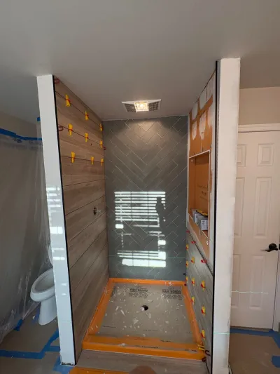 A shower under construction with herringbone tile, wood-look plank tile, and a protected floor pan mid-installation.