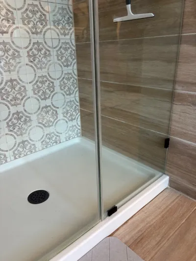 Close-up of a glass shower enclosure with patterned accent tile and wood-look porcelain tile walls.