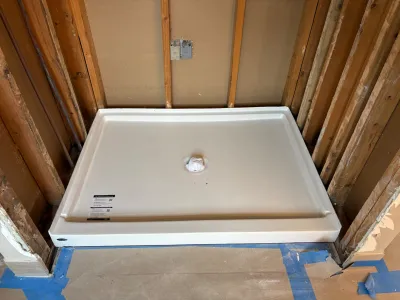 New shower base installed in a framed-out bathroom alcove during renovation, with exposed studs and rough plumbing.